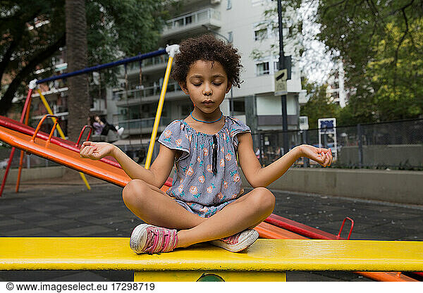 Adorable mixed race girl practicing meditation at playground outside