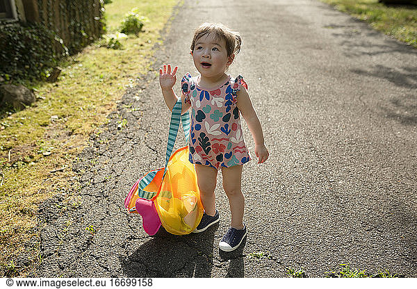 Adorable Toddler Girl Stands Outdoors Looking Up Holding Bag