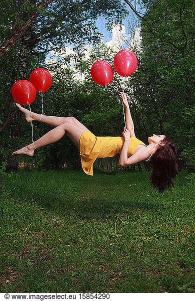 Adorable young brunette girl levitating on balloons in a park