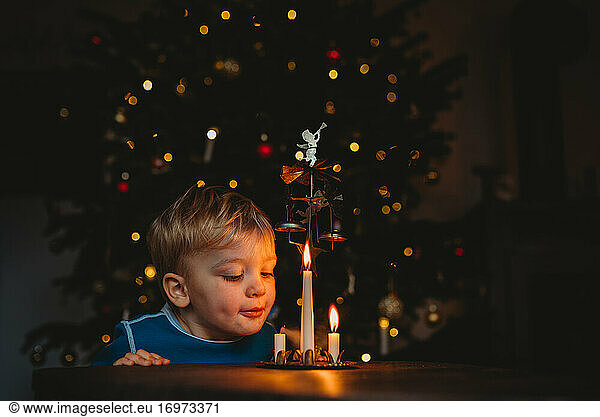 Adorable young child blowing candles with lit up Christmas tree behind
