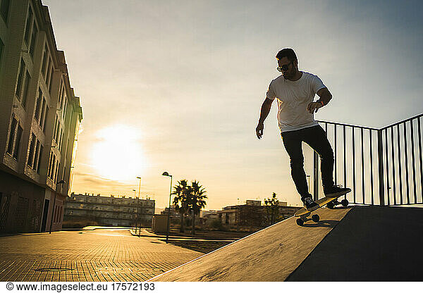 Adult man going down by ramp with a surf Skate at sunset
