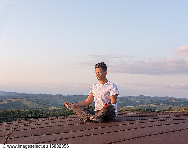 Adult man meditating on the terrace in the heat of the setting s