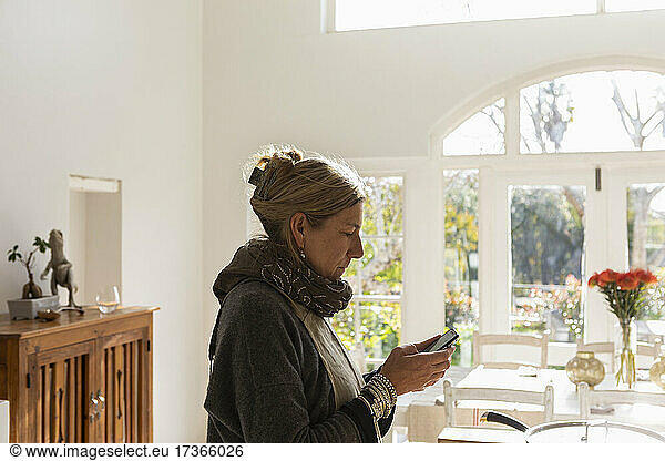 Adult woman in kitchen reading text on smart phone