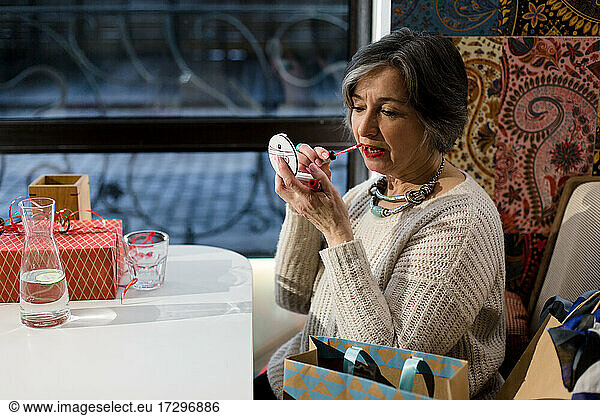 Adult woman sits at a table and tints her lips in a pocket mirror.