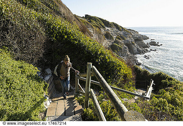 Adult woman walking up steps to the clifftop above a beach.