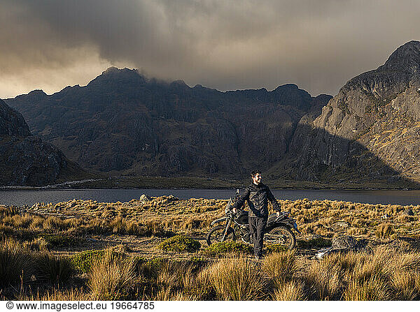 Adventure motorcyclist on mountain and lake of Peru at sunset