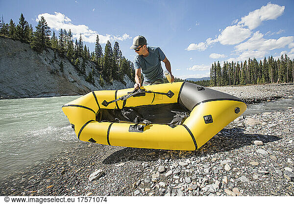 Adventurous man places packraft in river.