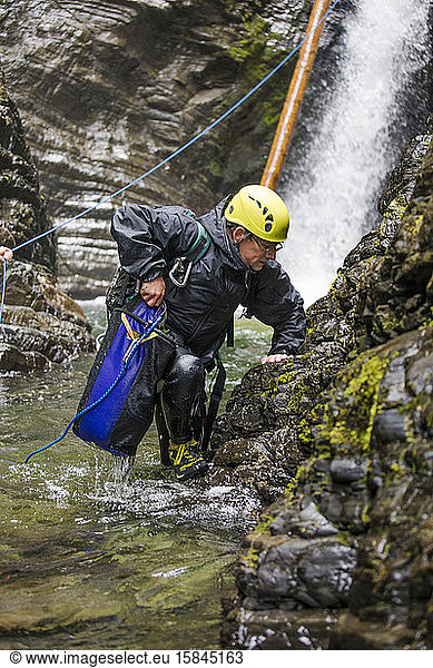 Adventurous man steps out of river after rappelling a waterfall.