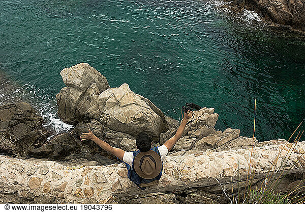 Adventurous man with photo camera and binoculars exploring a roc