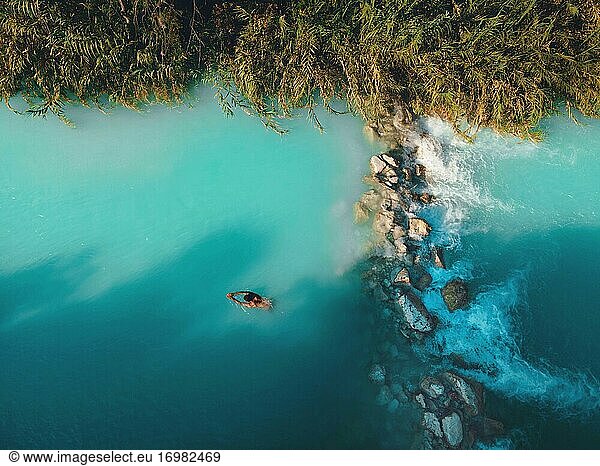 Aerial drone view of man swimming in tropical blue hot springs river