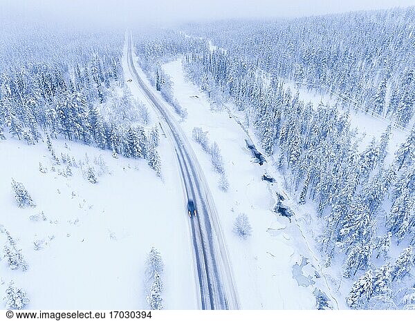 Aerial of car driving on a dangerous winter road in bad icy conditions next to frozen river and snow covered forest
