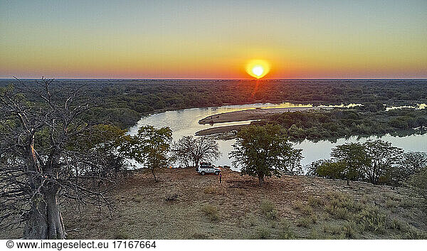 Aerial view of a jeep with a rooftop tent close to the river and a big baobab tree at sunset  Cunene river area  Angola