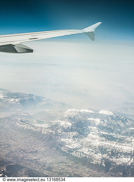 Aerial view of airplane wing and misty snow capped mountains