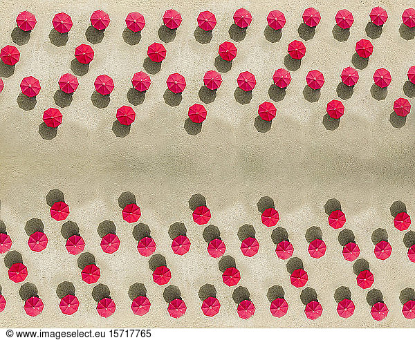 Aerial view of arrangement of red beach umbrellas on sandy beach