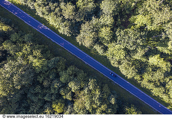 Aerial view of asphalt road cutting through green spruce forest in Swabian Alps