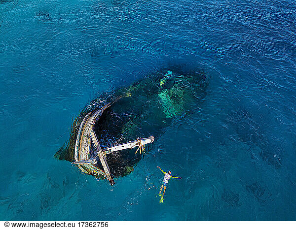 Aerial view of lone man snorkeling around sunken shipwreck