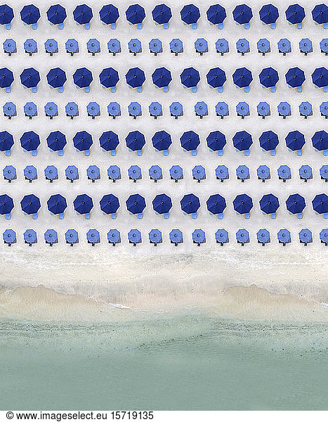 Aerial view of rows of blue beach umbrellas standing along sandy coastal beach