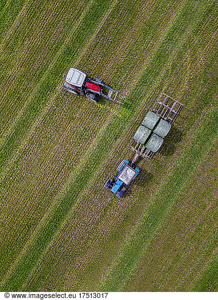 Aerial view of two tractors collecting hay bales in field