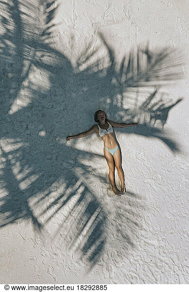 Aerial view of woman lying under tree shadow on sand