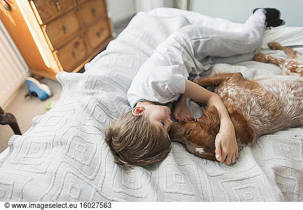 Affectionate boy cuddling dog on bed