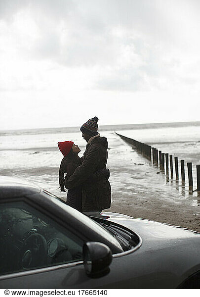 Affectionate couple in warm clothing hugging on wet winter beach