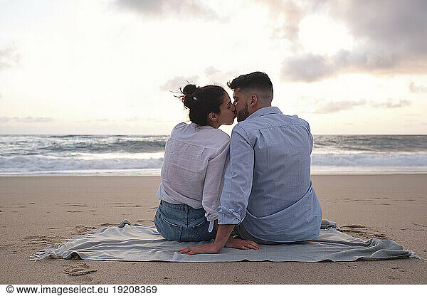 Affectionate couple kissing each other sitting on sand at beach