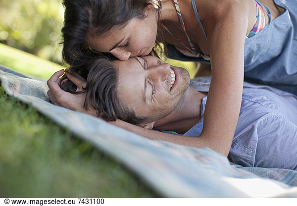 Affectionate couple laying on blanket in grass