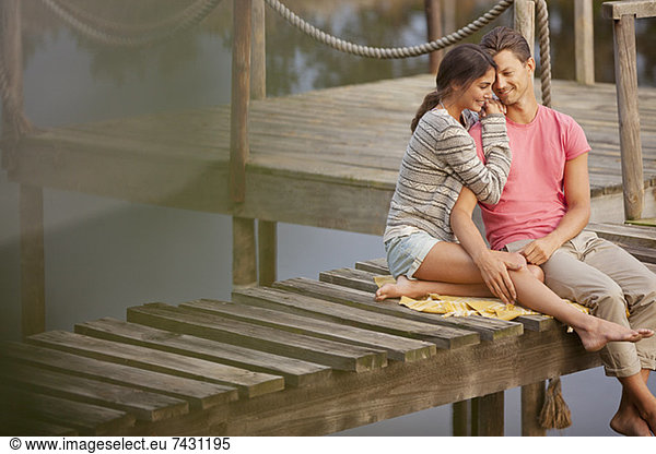 Affectionate couple sitting on dock over lake