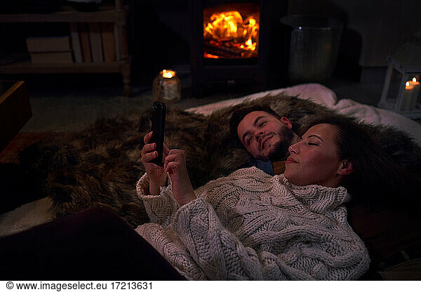 Affectionate couple using smart phone on blankets at cozy fireside
