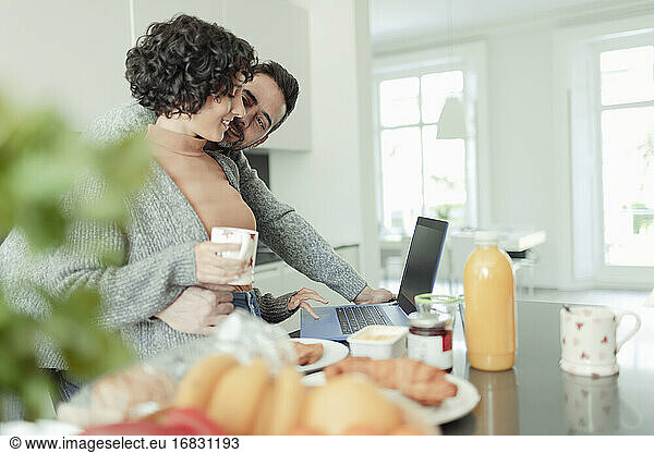 Affectionate couple working at laptop in morning kitchen