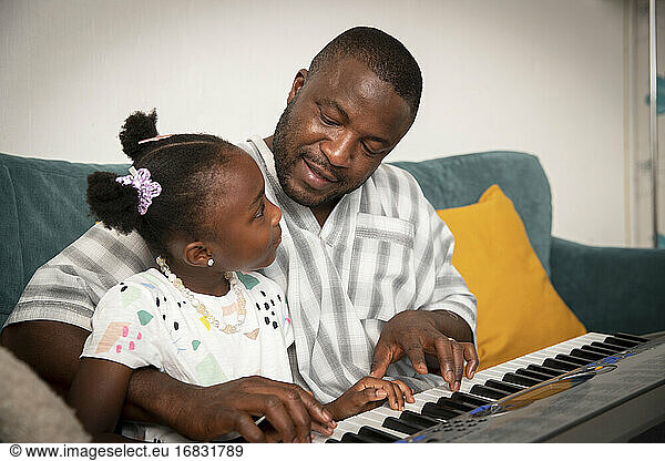 Affectionate father and daughter playing keyboard piano on sofa