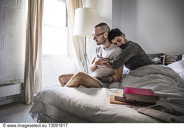 Affectionate gay couple sitting on bed at home