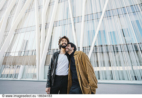 Affectionate gay couple standing in front of building