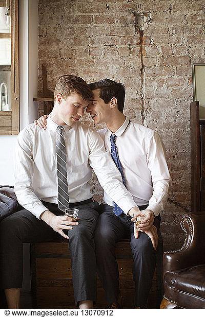 Affectionate gay couple with tequila shots sitting at home
