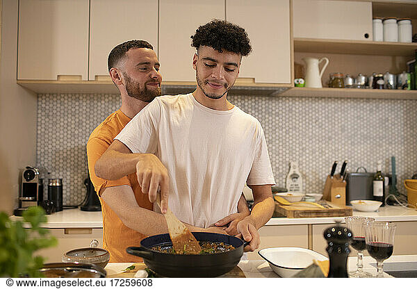 Affectionate gay male couple cooking in kitchen