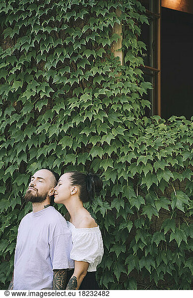 Affectionate hipster couple standing in front of green ivy plants