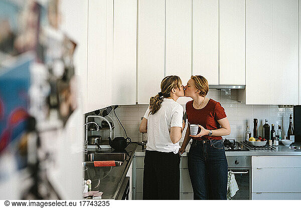 Affectionate lesbian couple kissing in kitchen at home