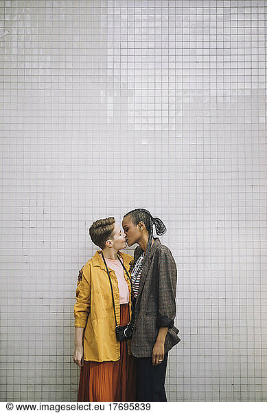 Affectionate lesbian couple kissing while standing against wall
