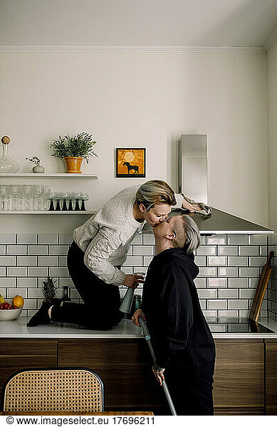 Affectionate lesbian women kissing each other while cleaning kitchen together at home