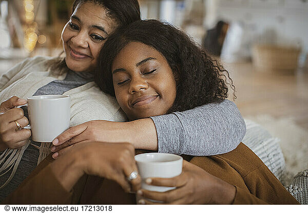 Affectionate mother and daughter cuddling with tea