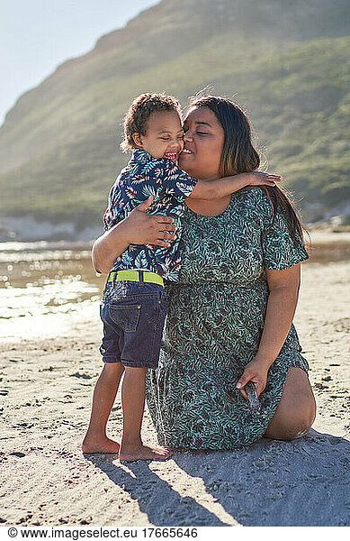 Affectionate mother hugging happy son on sunny beach