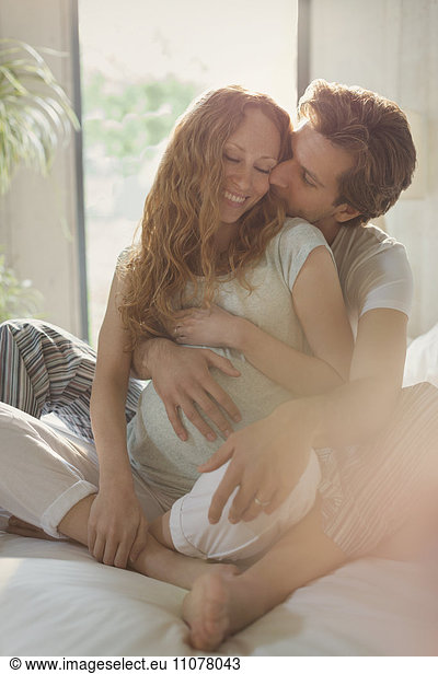 Affectionate pregnant couple kissing on bed
