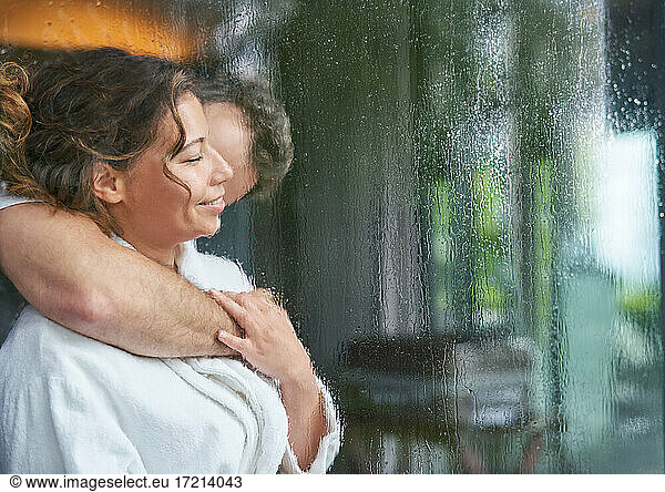 Affectionate romantic couple hugging at rainy window