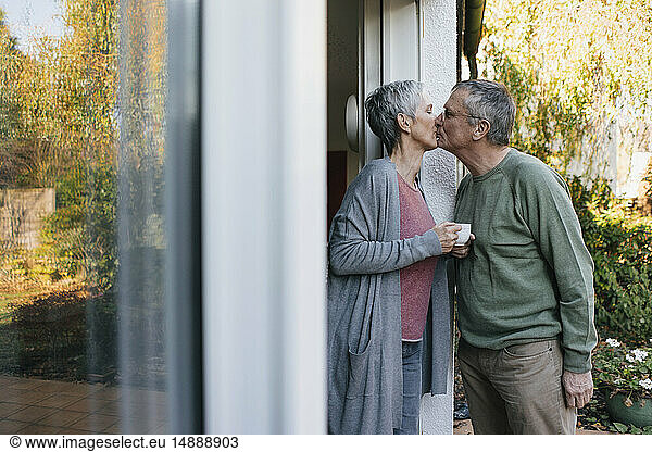 Affectionate senior couple kissing at terrace door