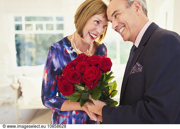 Affectionate well-dressed mature couple with rose bouquet