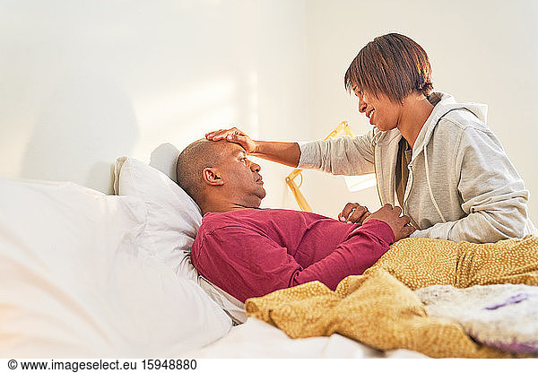 Affectionate wife checking fever of sick husband in bed