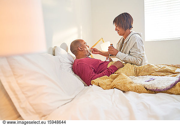 Affectionate wife giving cough syrup to sick husband in bed