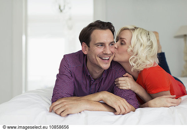 Affectionate wife kissing smiling husband on bed