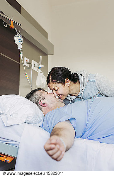 Affectionate woman visiting husband lying in hospital bed