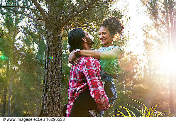 Affectionate young man holding happy girlfriend in sunny woods